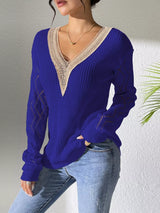 Woman wearing a blue V-neck hollow knit sweater with contrasting neckline, openwork long sleeves, and blue jeans.