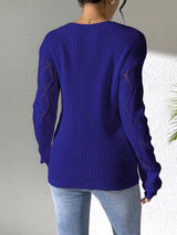 Woman wearing a blue V-neck hollow knit sweater with contrasting neckline, openwork long sleeves, and blue jeans.