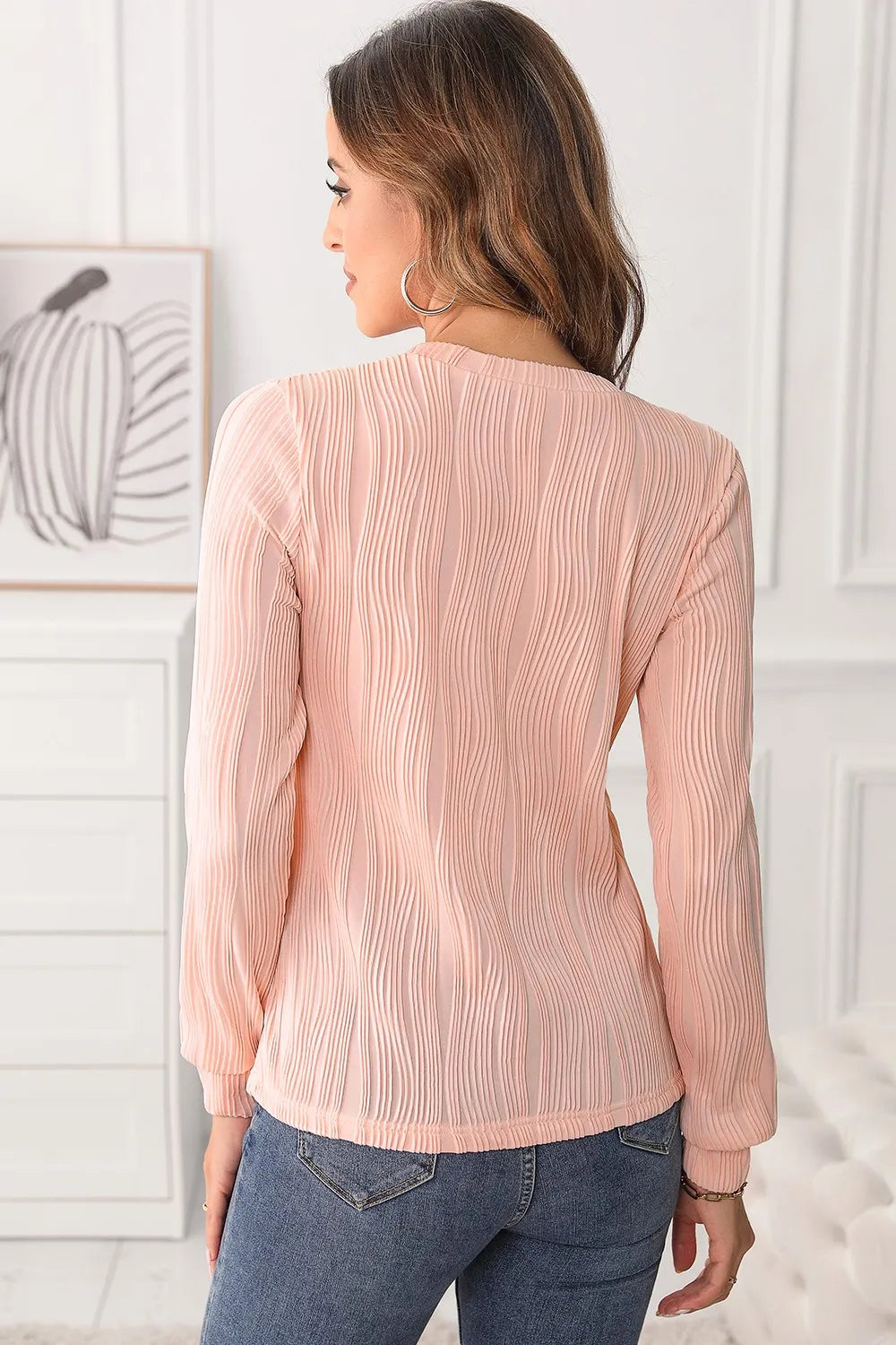 Woman wearing a blush pink textured round neck long sleeve blouse with dark-wash jeans.