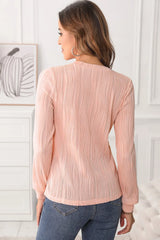 Woman wearing a blush pink textured round neck long sleeve blouse with dark-wash jeans.