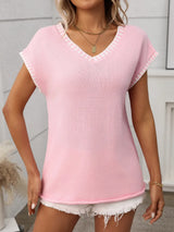 Woman wearing a blushing pink short sleeve knit top with white contrast trim along the V-neckline and sleeves.