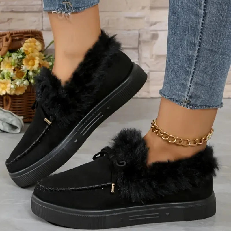 Black loafers with fur trim worn by a person, with a blurred background of flowers and a basket.