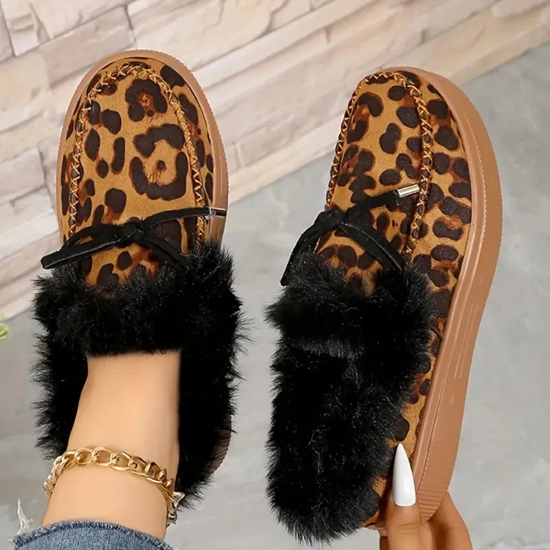 Leopard print slippers with black fur trim worn by a person on a neutral background