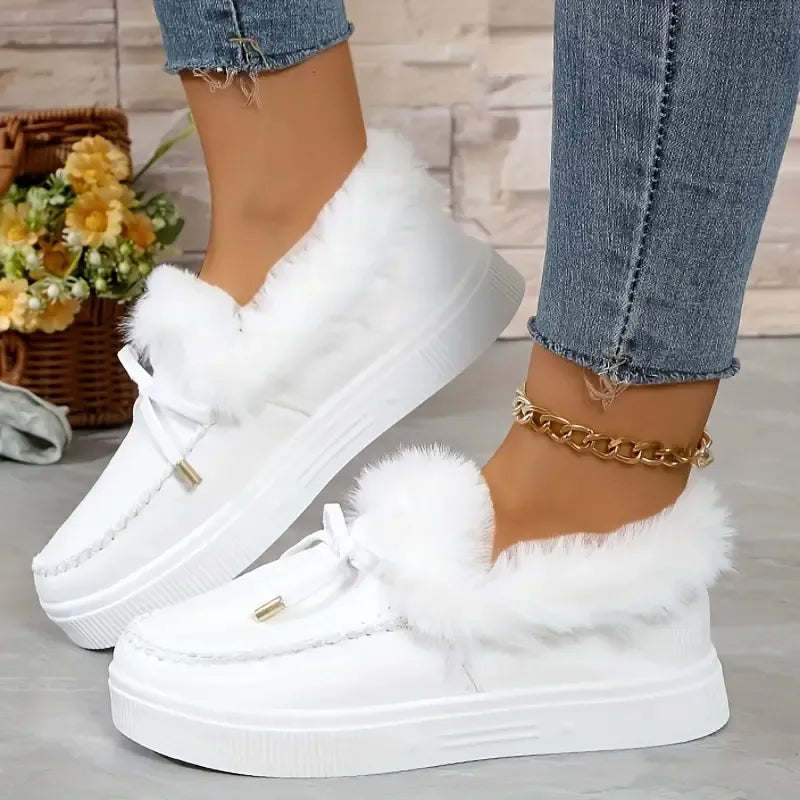 White sneakers with fluffy white laces worn with blue jeans on a light wooden floor.