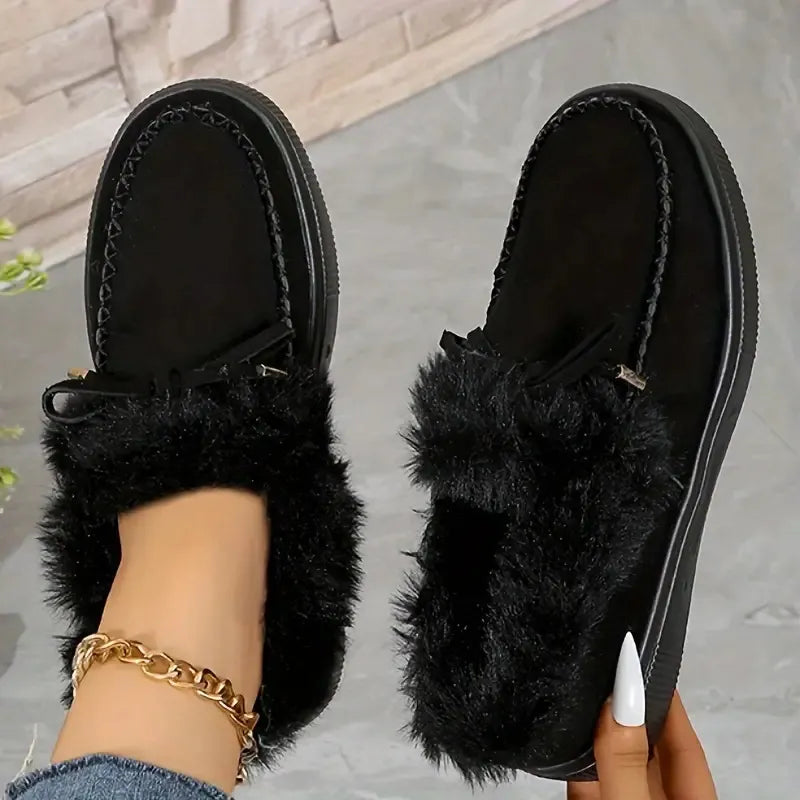 Black fuzzy slippers worn by a person on a neutral background