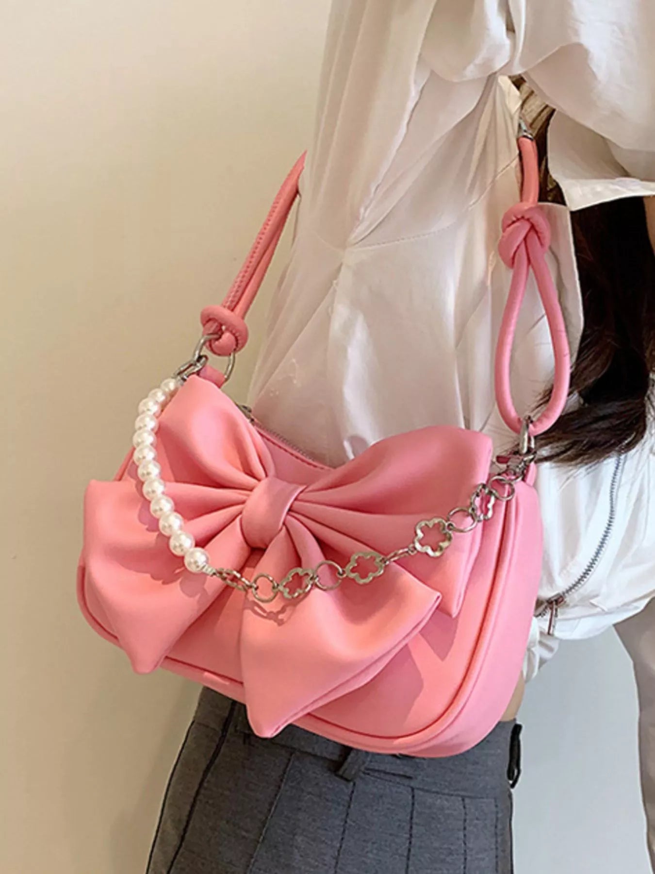 Pink handbag with a large bow and pearl chain held by a person wearing a white shirt.