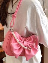 Pink handbag with a large bow and pearl details worn by a person.