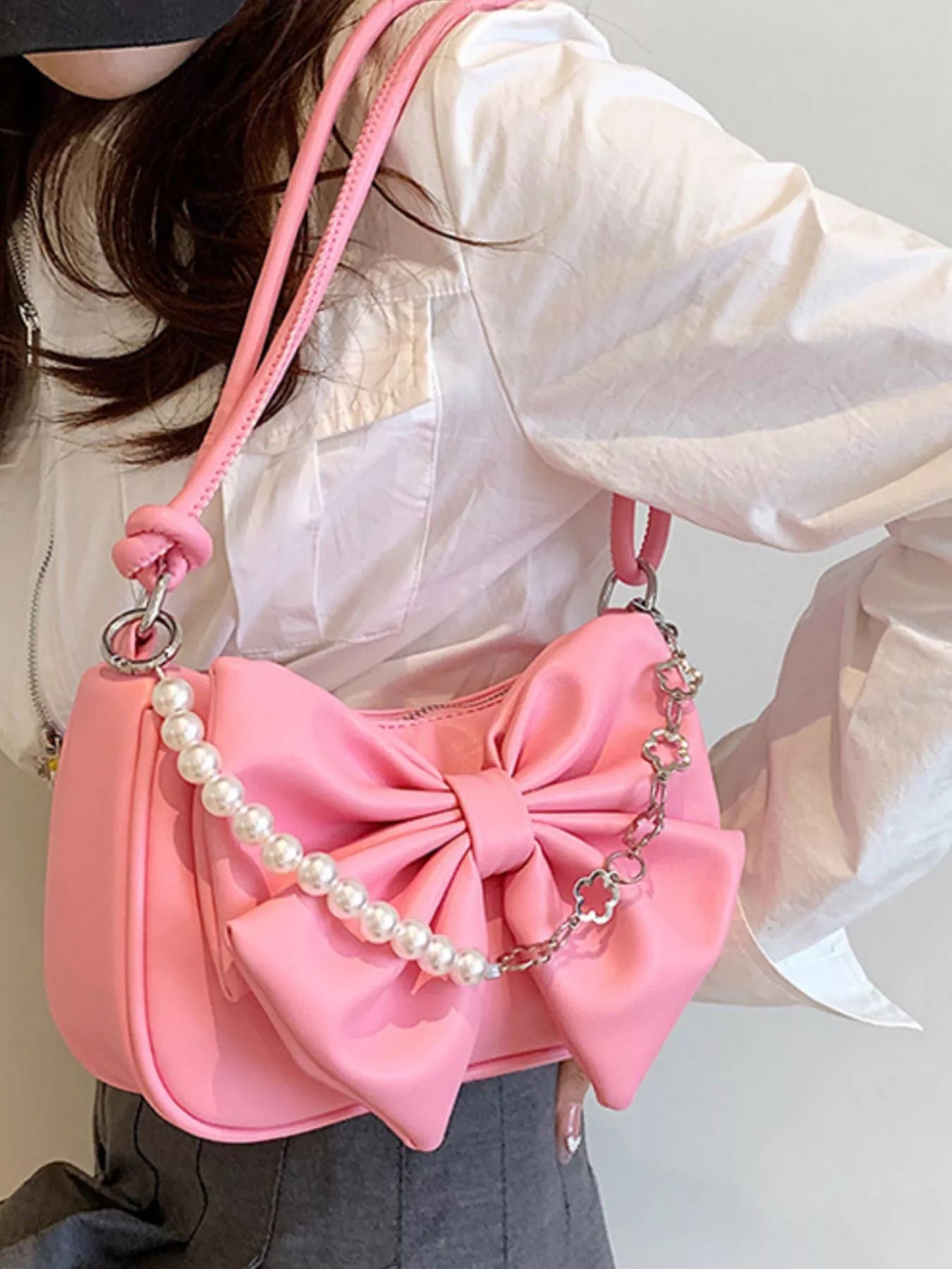 Pink handbag with a large bow and pearl details held by a person wearing a white jacket.