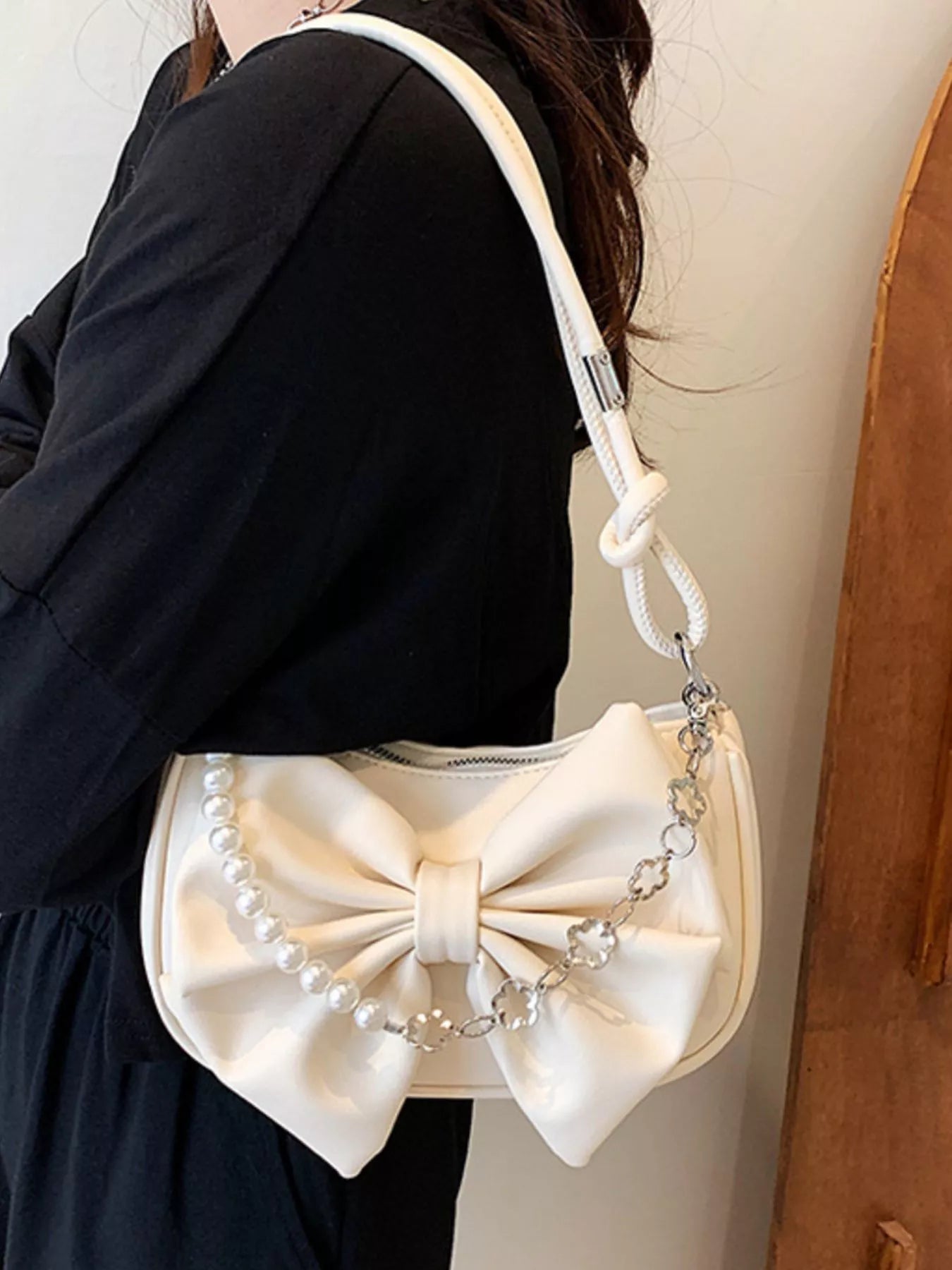White handbag with a large bow design worn by a person against a neutral background