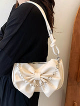 White handbag with a large bow design worn by a person against a neutral background
