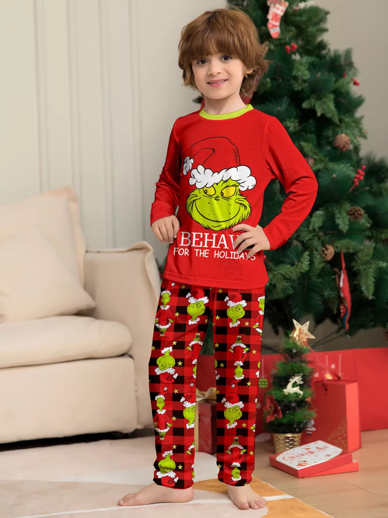 Boy wearing red Grinch-themed Christmas pajama sets with green character graphics and coordinating red plaid holiday pants.