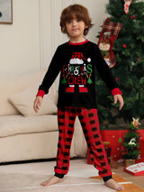 Boy wearing matching Christmas Crew graphic pajama sets with black long-sleeve tops and red buffalo plaid pants.