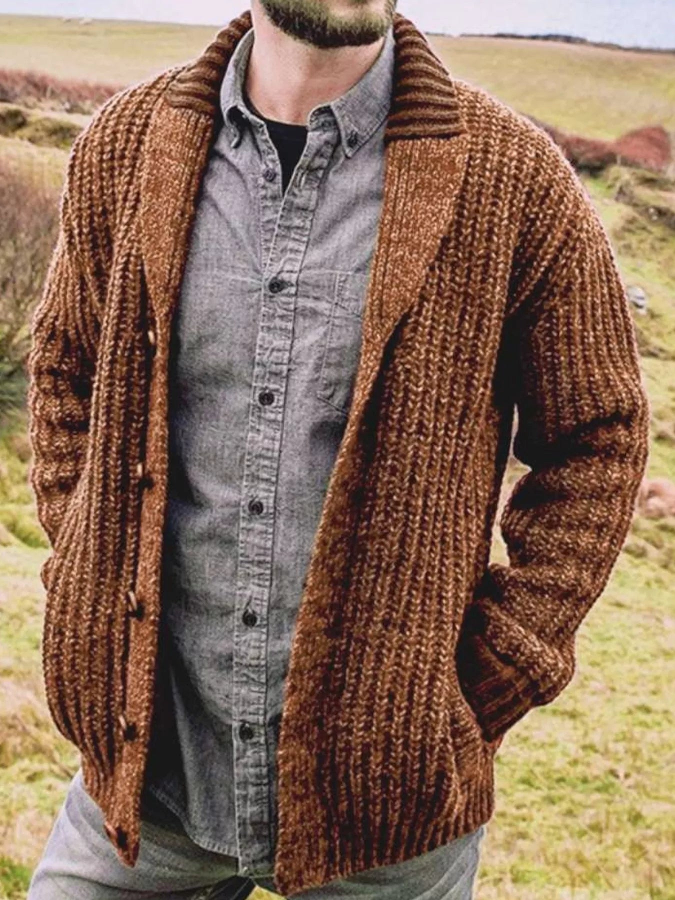 Men's brown chunky knit shawl collar cardigan with button-front closure, ribbed texture, and front pockets, layered over a gray button-down shirt.