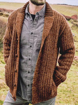 Men's brown chunky knit shawl collar cardigan with button-front closure, ribbed texture, and front pockets, layered over a gray button-down shirt.