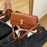 Brown rectangular crossbody handbag with a gold turn-lock buckle and adjustable shoulder strap displayed on a modern tabletop.