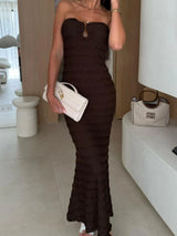 Woman wearing a brown sweetheart neck tube maxi dress with ruched detailing and a subtle cutout, styled with an ivory clutch for an elegant evening look.