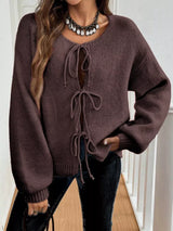 Woman wearing a brown tie-front long sleeve knit cardigan with three bow ties paired with blue jeans.
