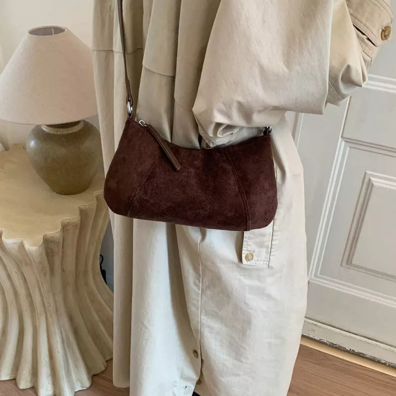 Brown suede vintage-style shoulder bag with a minimalist silhouette paired with a neutral outfit.