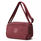 Small burgundy nylon crossbody bag with an adjustable matching strap, silver-tone buckle, zippered top closure, and front pocket detail.