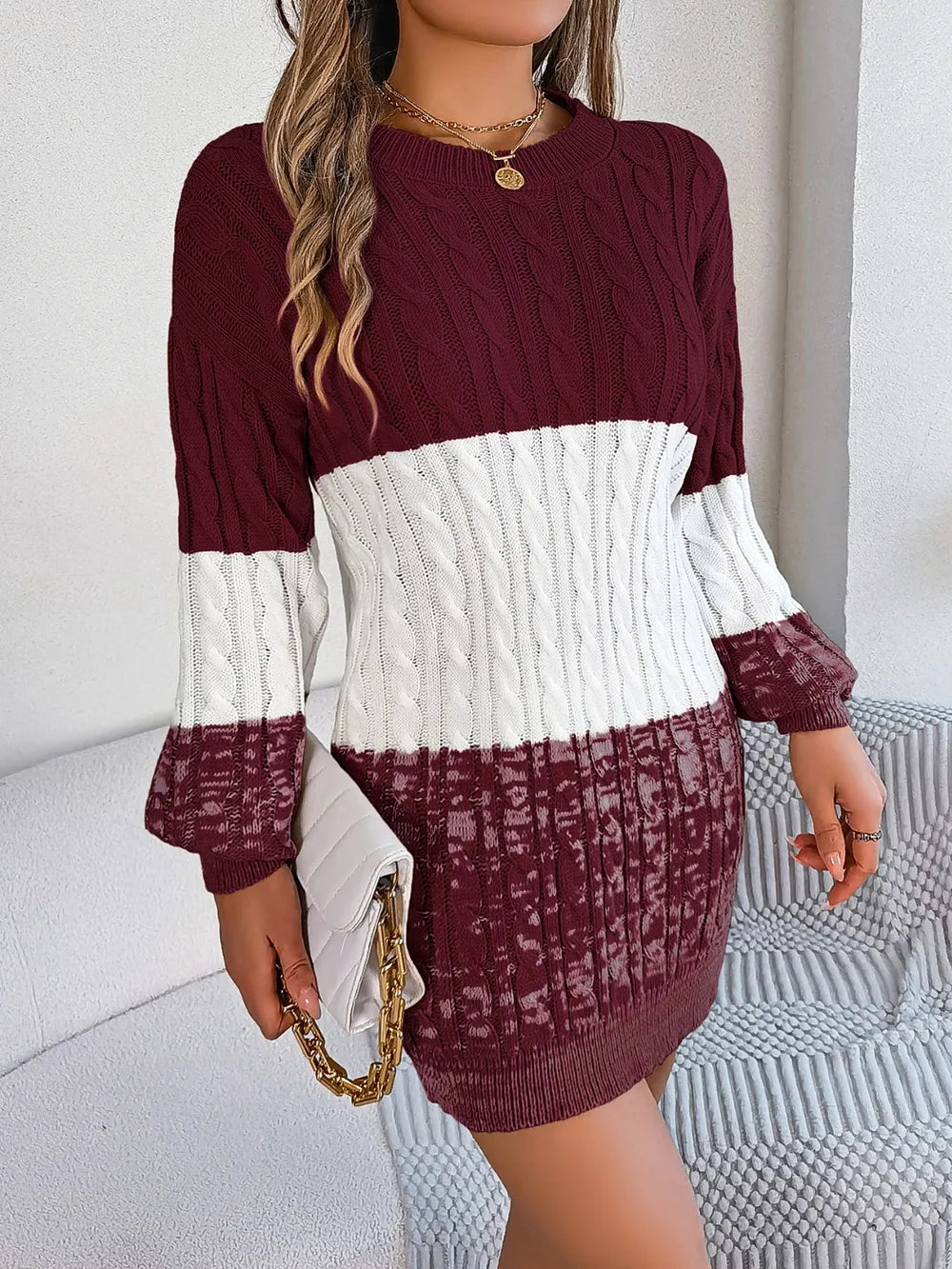 Women's burgundy and ivory cable-knit color block sweater dress with round neckline, long sleeves, and patterned knit hem.