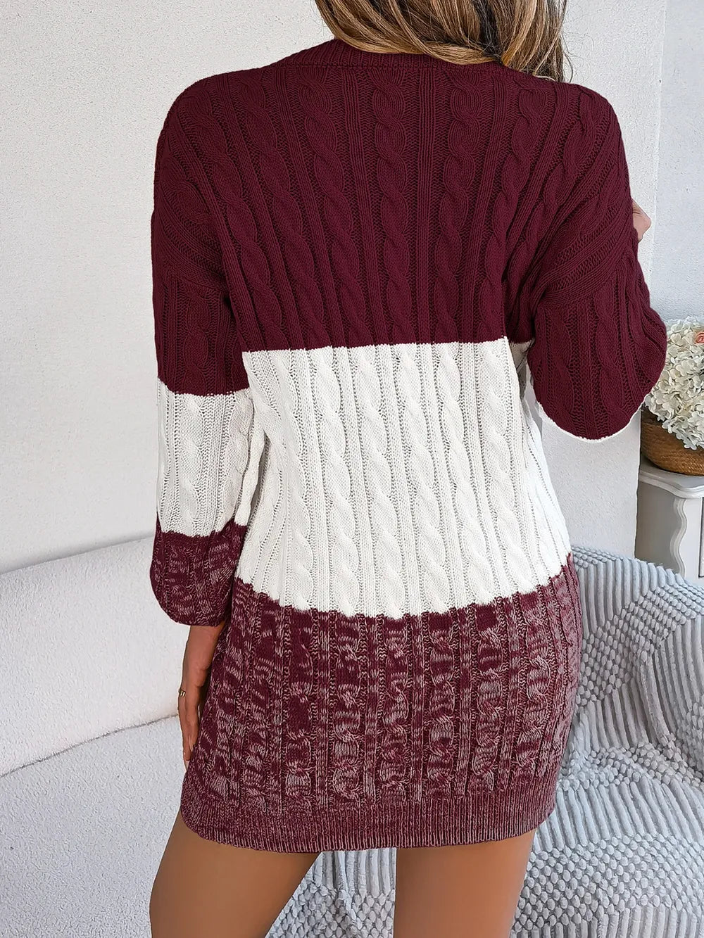Women's burgundy and ivory cable-knit color block sweater dress with round neckline, long sleeves, and patterned knit hem.