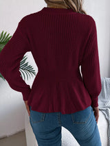 Woman wearing a burgundy cable knit round neck peplum sweater with long sleeves and blue jeans.