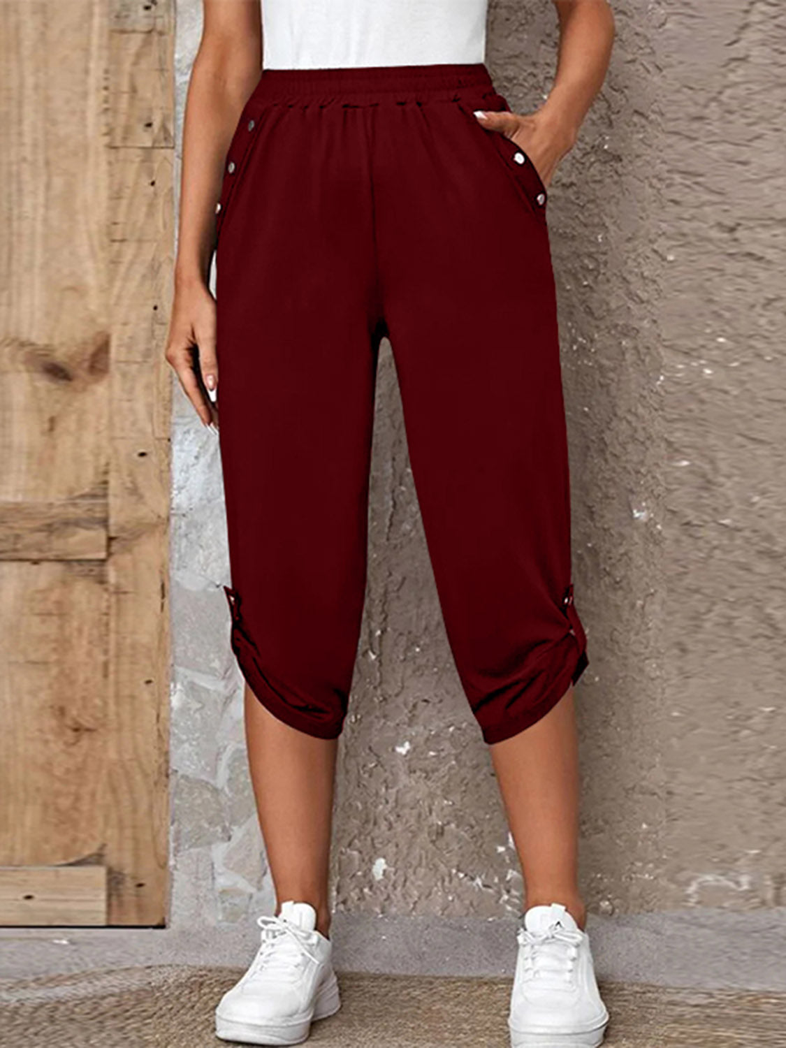 Model wearing burgundy roll-tab capri pants with side pockets and white sneakers for a casual outdoor look.