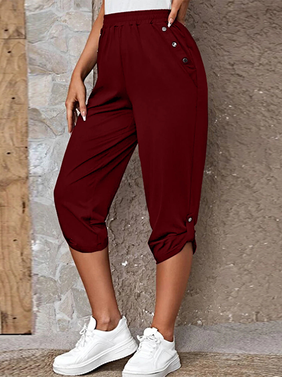 Model wearing burgundy roll-tab capri pants with side pockets and white sneakers for a casual outdoor look.