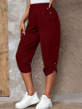 Model wearing burgundy roll-tab capri pants with side pockets and white sneakers for a casual outdoor look.