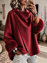 Woman wearing burgundy asymmetric outerwear with plush faux fur cuffs and button detail, styled with distressed white jeans.
