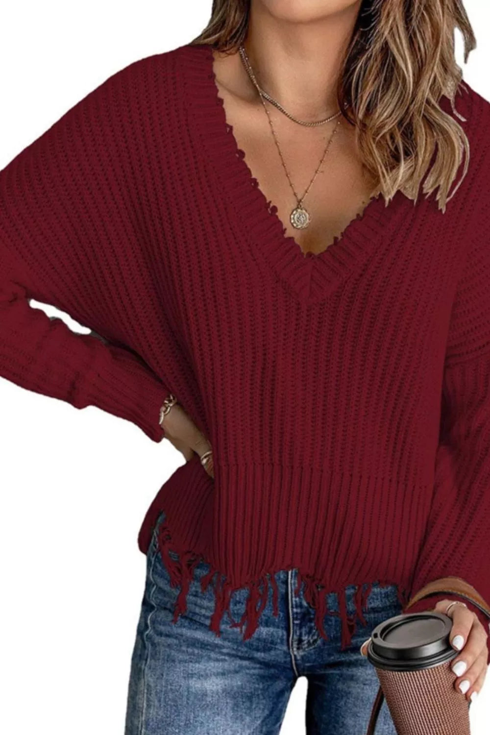 Woman wearing a burgundy ribbed V-neck sweater with distressed raw hem and blue jeans.