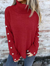 Woman wearing a burgundy ribbed turtleneck sweater with decorative button sleeves and jeans.