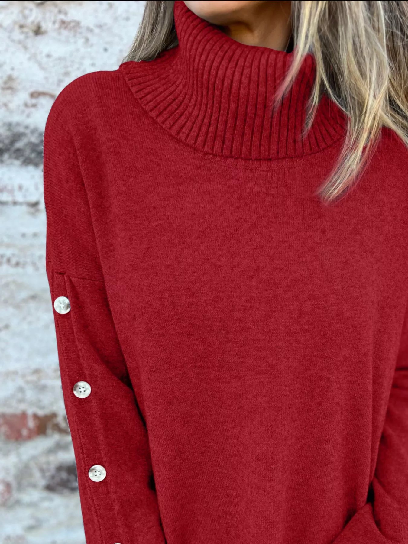 Woman wearing a burgundy ribbed turtleneck sweater with decorative button sleeves and jeans.