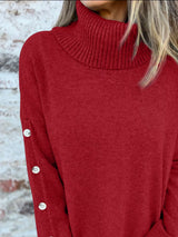 Woman wearing a burgundy ribbed turtleneck sweater with decorative button sleeves and jeans.