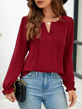 Woman wearing a burgundy notched neck long sleeve blouse with flounce cuffs styled with light-wash jeans and a black handbag.