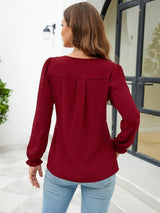 Woman wearing a burgundy notched neck long sleeve blouse with flounce cuffs styled with light-wash jeans.