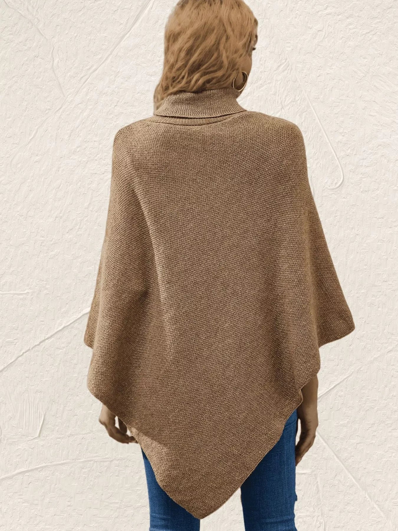 Back view of women's khaki knit turtleneck poncho pullover showing the loose draped silhouette and pointed hem, styled with blue jeans.