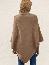 Back view of women's khaki knit turtleneck poncho pullover showing the loose draped silhouette and pointed hem, styled with blue jeans.