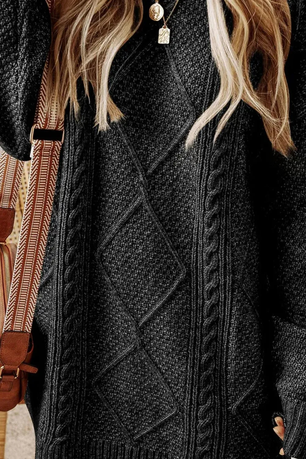 Woman wearing a black cable knit long sleeve sweater dress styled with knee-high brown boots and layered gold necklaces.