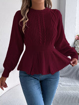 Woman wearing a burgundy cable knit round neck peplum sweater with long sleeves and blue jeans.