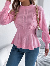Woman wearing a pink cable knit round neck peplum sweater with long sleeves and blue jeans.