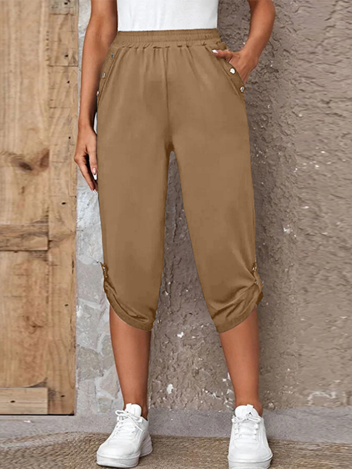 Model wearing camel roll-tab capri pants with side pockets and white sneakers for a casual outdoor look.