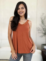 Woman wearing a caramel-colored Basic Bae lace-detail V-neck cami with delicate lace trim and cutout accents, styled with dark-wash jeans for a chic casual look.