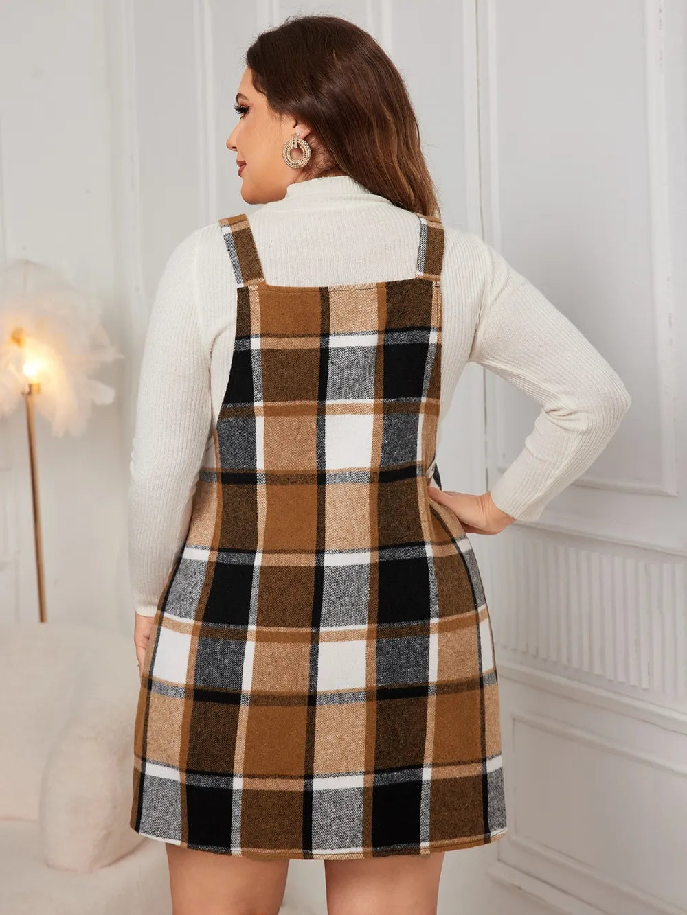 Woman wearing the Honey Plus Size Plaid Wide Strap Overall Dress layered over a cream mock neck sweater with a black felt hat, stylish plus size plaid fall dress from Chic Mystik Boutique.