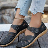 Black sandals with brown soles worn by a person on a wooden surface.