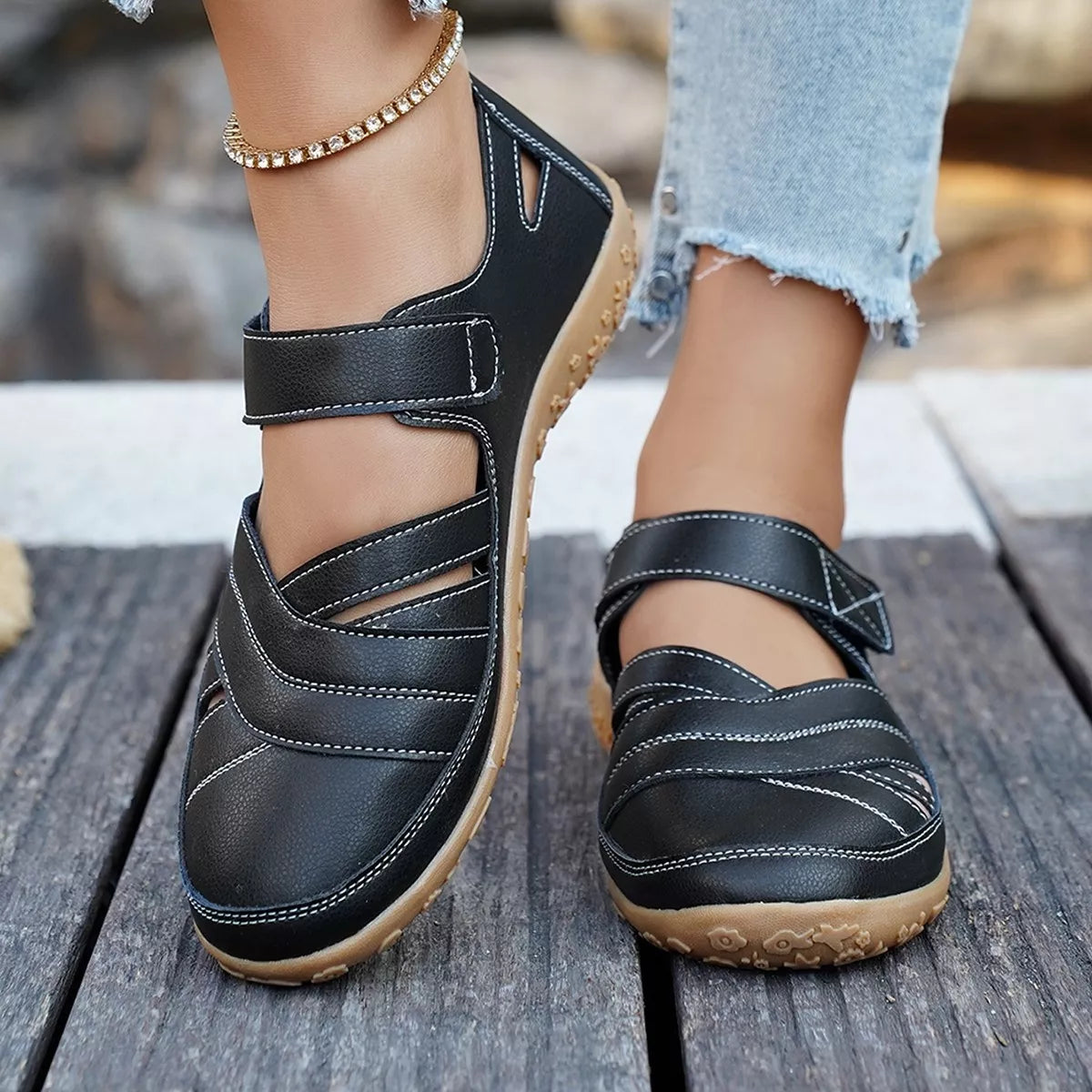 Black sandals with brown soles worn on a wooden floor
