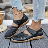 Black sandals with brown soles worn by a person on a wooden surface.