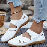 White sandals with brown soles worn by a person on a wooden floor.
