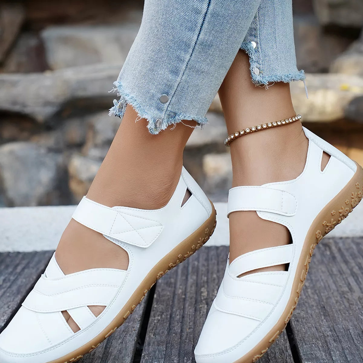 White sandals with brown soles worn with light blue jeans on a wooden surface.