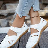 White sandals with brown soles worn with light blue jeans on a wooden surface.